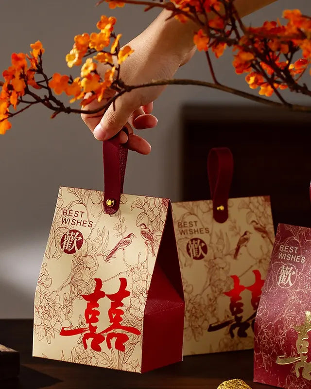  Double Happiness Chinese Wedding Favor Box with red handles and Chinese characters, held by a hand with orange flowers.