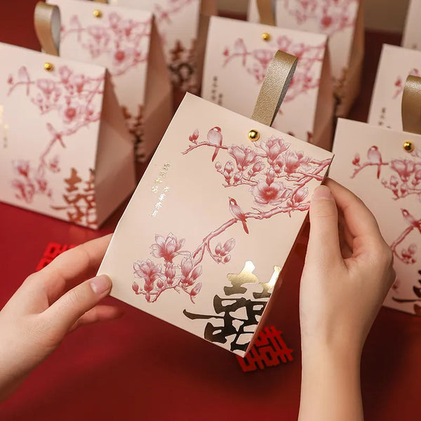 Person holding a red red and gold Double Happiness Wedding Favor Box  with Blossom & Bird desigin on a red background