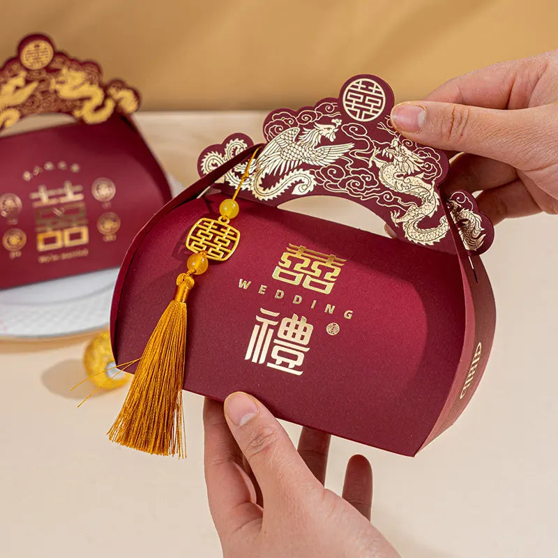 Red Dragon & Phoenix Double Happiness Chinese Wedding Favor Boxes with gold tassel and decorative elements, held by a hand against a beige background.