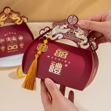 Red Dragon & Phoenix Double Happiness Chinese Wedding Favor Boxes with gold tassel and decorative elements, held by a hand against a beige background.