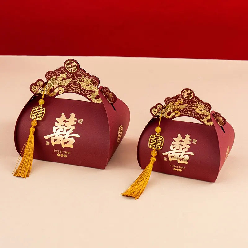 Two red Dragon & Phoenix Double Happiness Chinese Wedding Favor Boxes with gold decorations and tassels on a red background