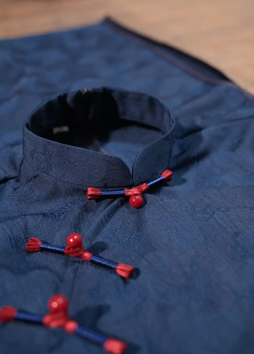 Close-up of a Elegant Blue Jacquard Butterfly Cheongsam – Mid-Length Modern Qipao  with red and blue buttons on a wooden surface