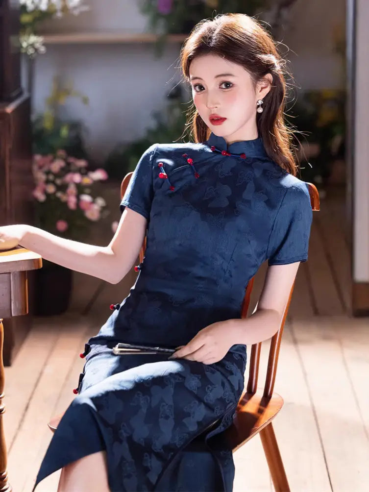 Woman in a Elegant Blue Jacquard Butterfly Cheongsam – Mid-Length Modern Qipao  sitting on a wooden chair indoors.