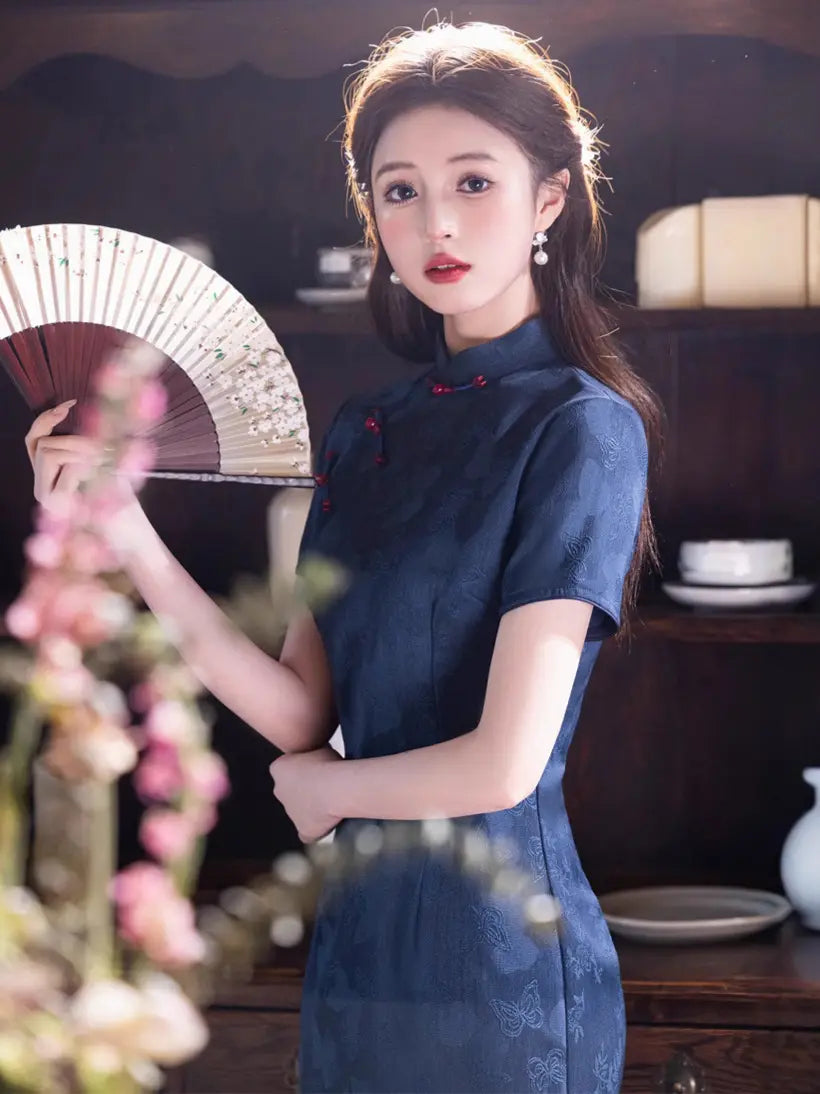 Woman in a Elegant Blue Jacquard Butterfly Cheongsam – Mid-Length Modern Qipao  holding a fan in a traditional setting