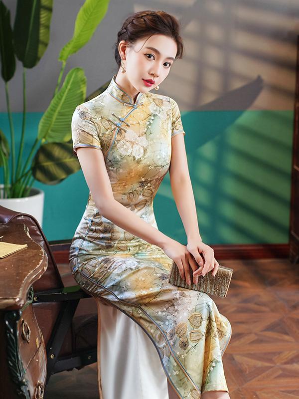 Woman in a Elegant Floral Mulberry Silk Qipao Cheongsam Dress  sitting indoors with plants and a wooden table in the background