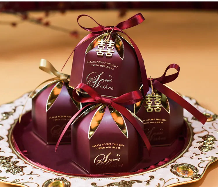 Elegant Wedding Favor Boxes with Double Happiness Charm with red ribbons on a decorative plate.