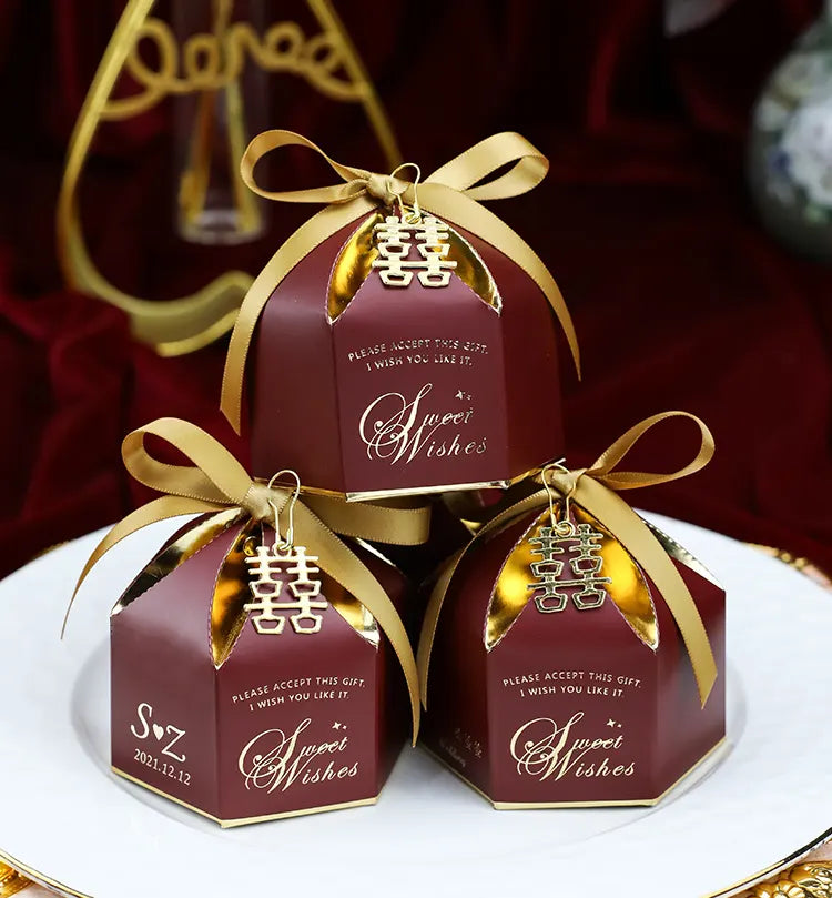 Three red  Wedding Favor Boxes with Double Happiness Charm with gold ribbons and 'Sweet Wishes' text on a white surface.