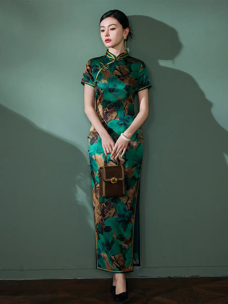 Woman in a Emerald Green Floral Silk Chinese Qipao Cheongsam Dress  holding a brown handbag against a green wall.