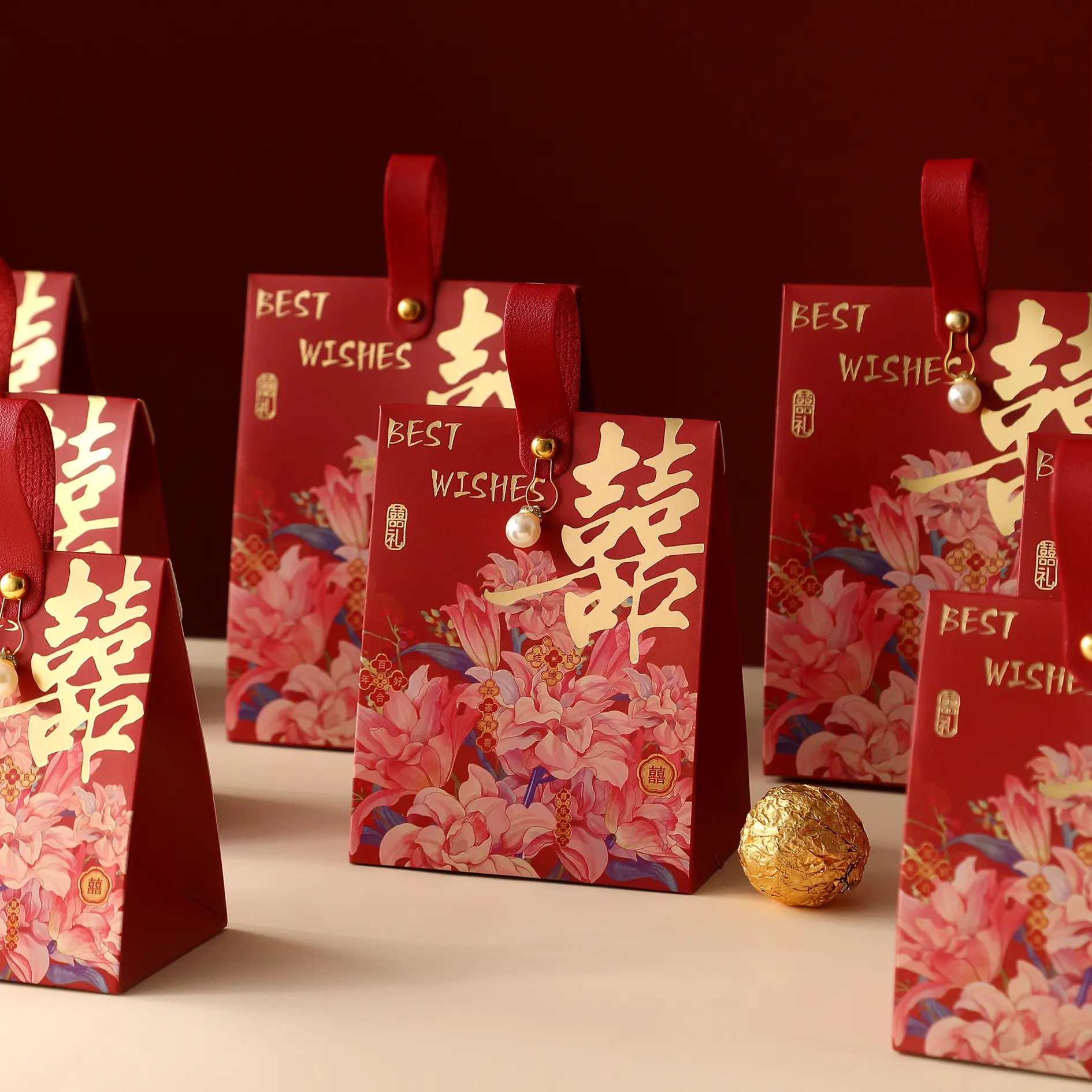 Red Chinese wedding gift bags with floral prints and gold calligraphy, arranged on a light surface against a dark red background.