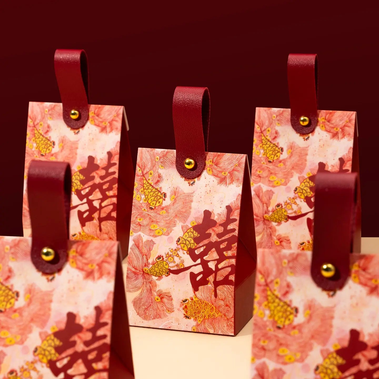 Four red and pink Floral & Koi Fish Double Happiness Wedding Favor Boxes With Handle with dark red handles and gold-tone metal snaps, decorated with large red Chinese double happiness symbols and gold berry motifs, set against a dark red background.
