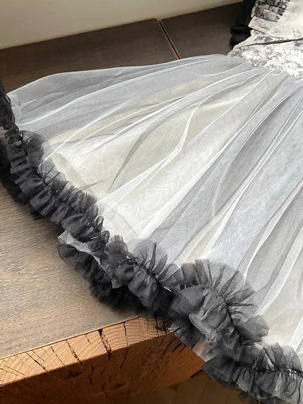 A close-up of a sheer white tulle skirt or fabric panel with layered ruffles along the edge, laid on a wooden surface.