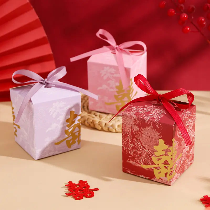 Three Gold Foil Double Happiness Chinoiserie Wedding Favor Boxes   with ribbons on a beige surface with a red background
