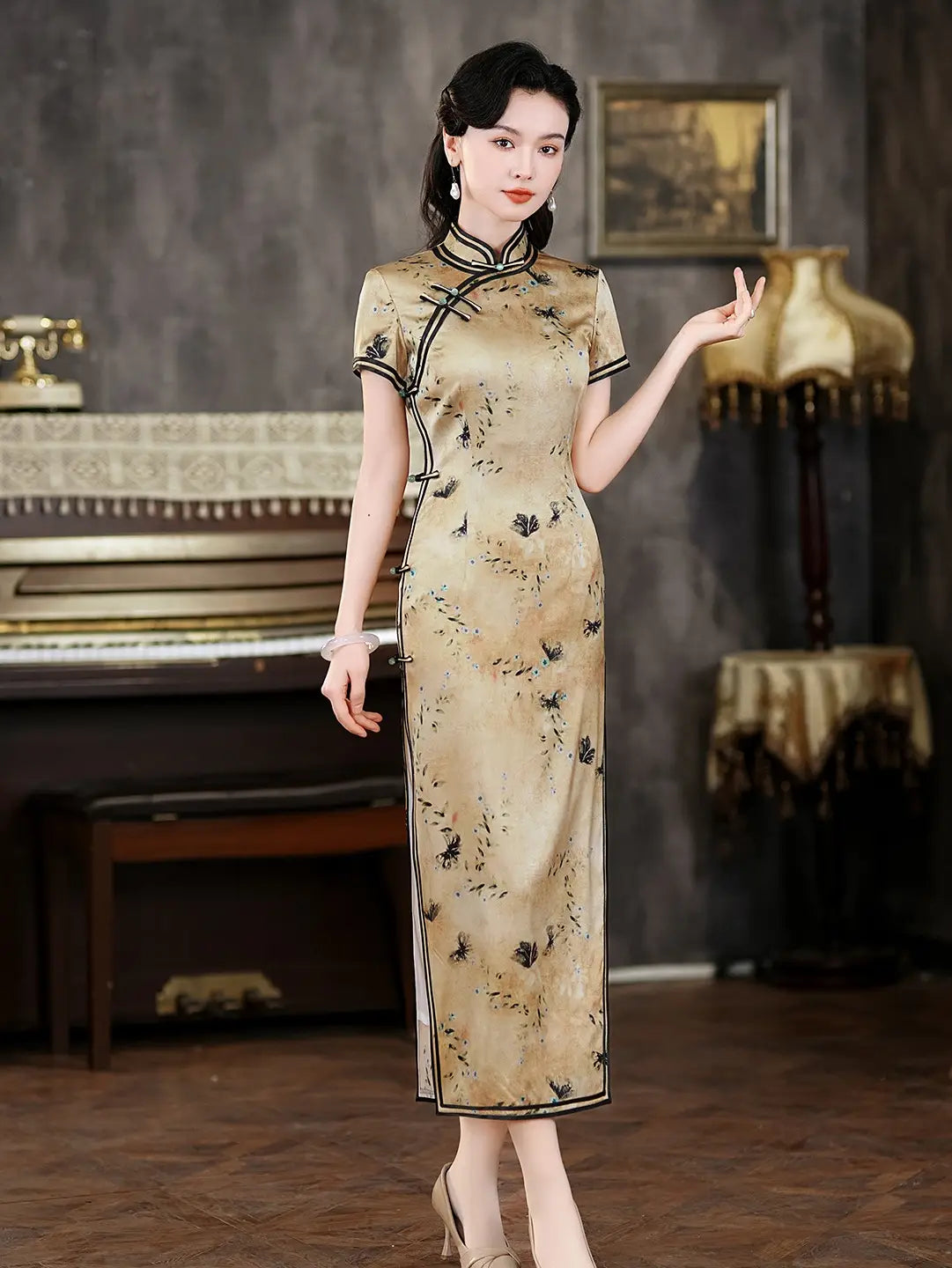 Woman in a traditional Gold Mulberry Silk cheongsam Dress with Black Floral Print  standing in a vintage room with a piano and lamp.