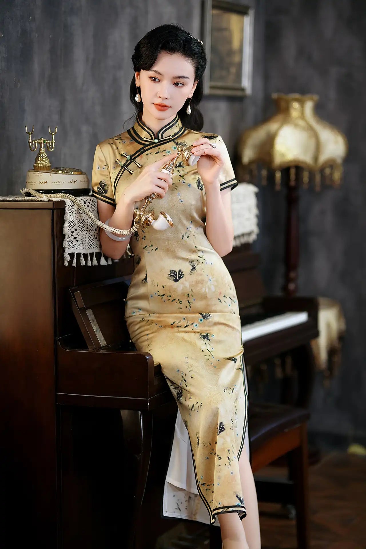 Woman in a traditional Golden Mulberry Silk Qipao Dress with Black Floral Print  sitting at a piano in a vintage room.