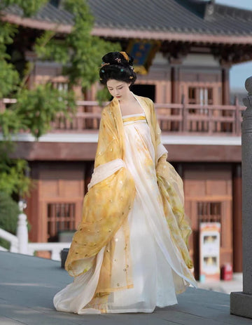 Woman in traditional yellow and Golden Traditional Chinese Tang Dynasty Hanfu Dress Set  standing in front of a wooden building.