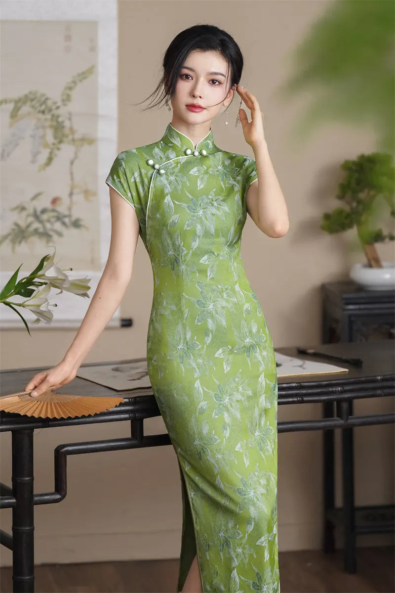 Woman in a Green Floral  Cap Sleeve Modern Qipao Cheongsam Dressstanding in a room with a painting and plants.