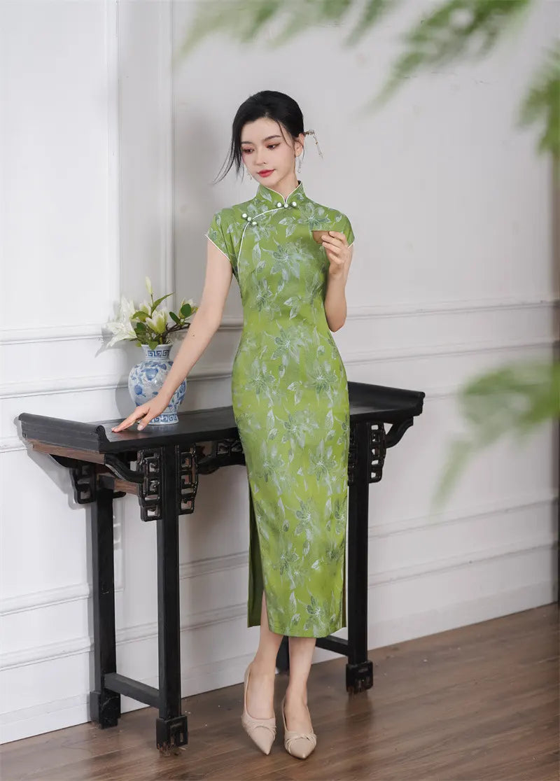 Woman in a Green Floral  Cap Sleeve Modern Qipao Cheongsam Dress standing next to a black table with a white wall background