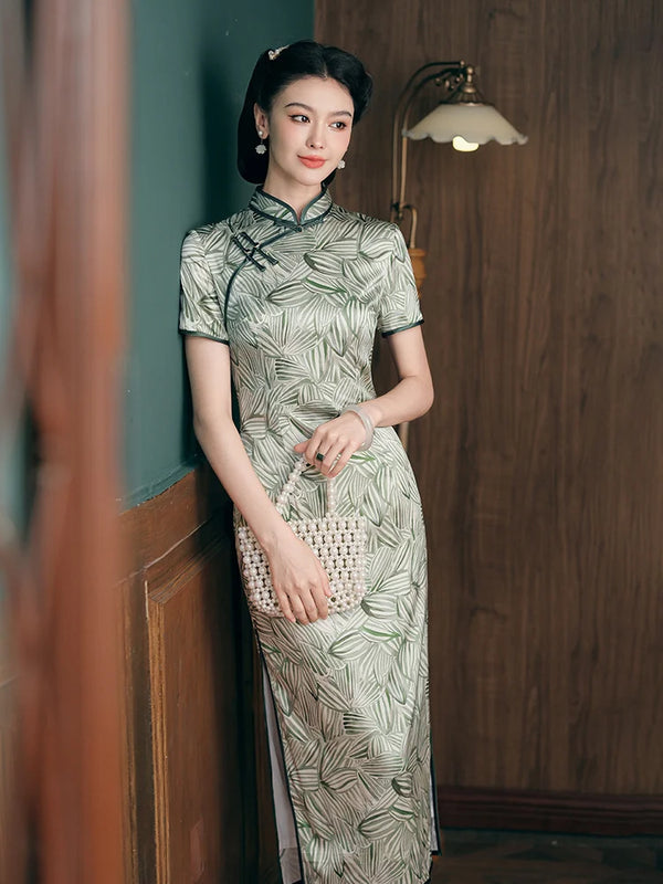 Woman in a Green Leaf Print Silk Long Qipao Dress holding a woven handbag indoors.
