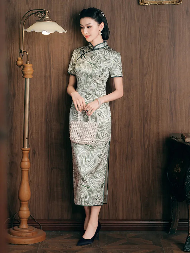 Woman in a Green Leaf Print Silk Long Qipao Dress  holding a handbag against a wooden wall.
