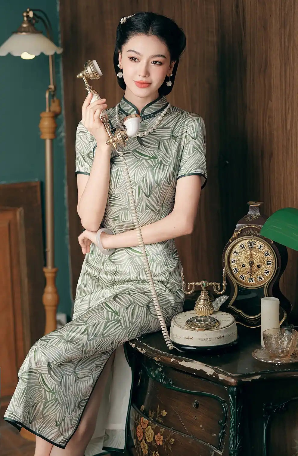 Woman in a Green Leaf Print Silk Long Qipao Dress dress holding a vintage phone in an elegant room.