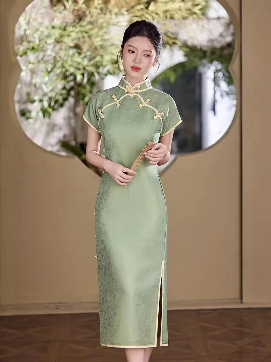 Woman in a green traditional  Song Brocade Full-Opening  Qipao Dress holding a fan, standing in front of a decorative mirror.