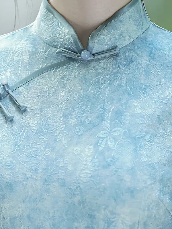 Close-up of a person wearing a light blue traditional Chinese-style blouse with a tonal floral jacquard pattern, a mandarin collar, and a tie closure.