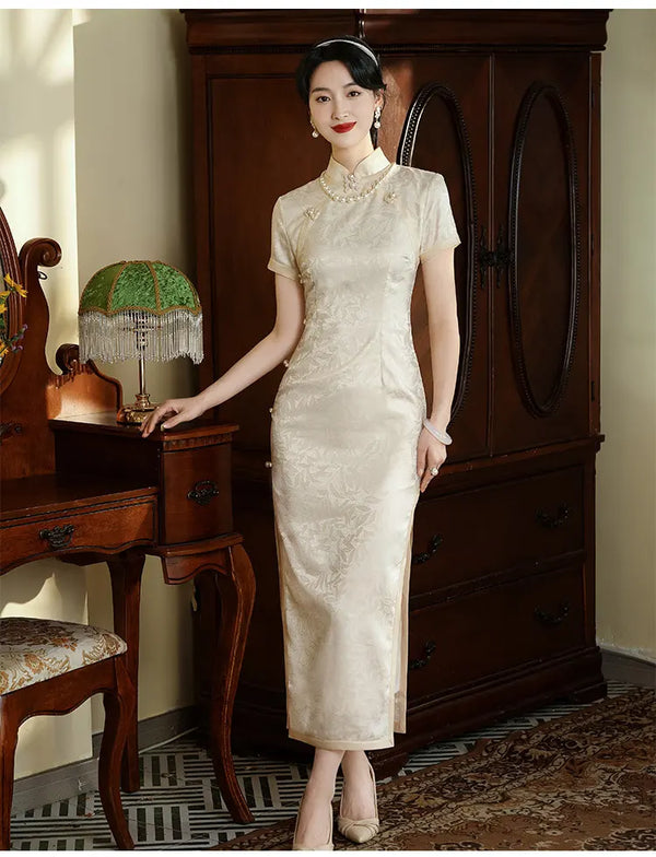 Woman in a Ivory White Floral Jacquard Short Sleeve Qipao Dress standing in a room with wooden furniture and a lamp.