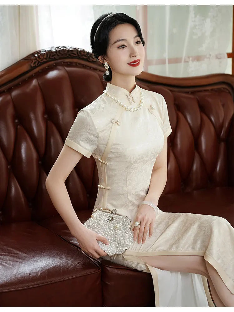 Woman in a Ivory White Floral Jacquard Short Sleeve traditional chinese  Qipao outfit sitting on a brown leather couch.