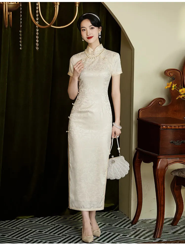 Woman in a Ivory White Floral Jacquard Short Sleeve traditional chinese  Qipao Dress  standing in a room with a dark curtain and wooden furniture.