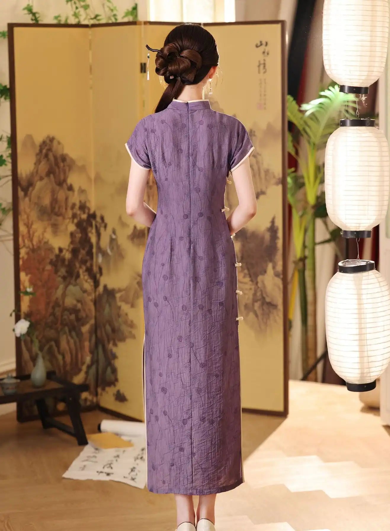 Woman in a long purple  Lavender Floral Short Sleeves Jacquard Qipao Dress  standing in a room with traditional decor elements.