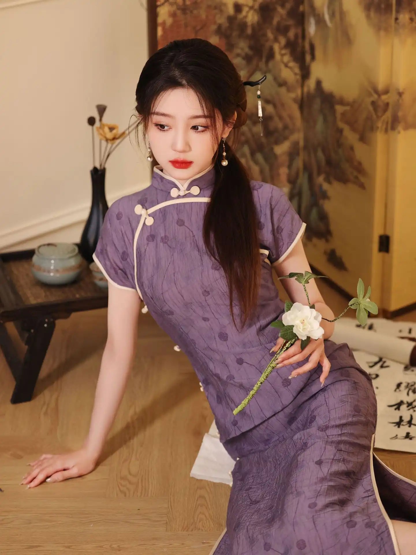 Woman in a traditional purple Lavender Floral Short Sleeves Jacquard Qipao Dress outfit holding a white flower in a room with classical decor.