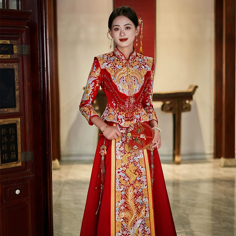 Woman in a traditional red and gold Luxury Embroidered Dragon & Phoenix Bridal Wedding Qun Kwa dress with intricate patterns in an elegant interior setting.