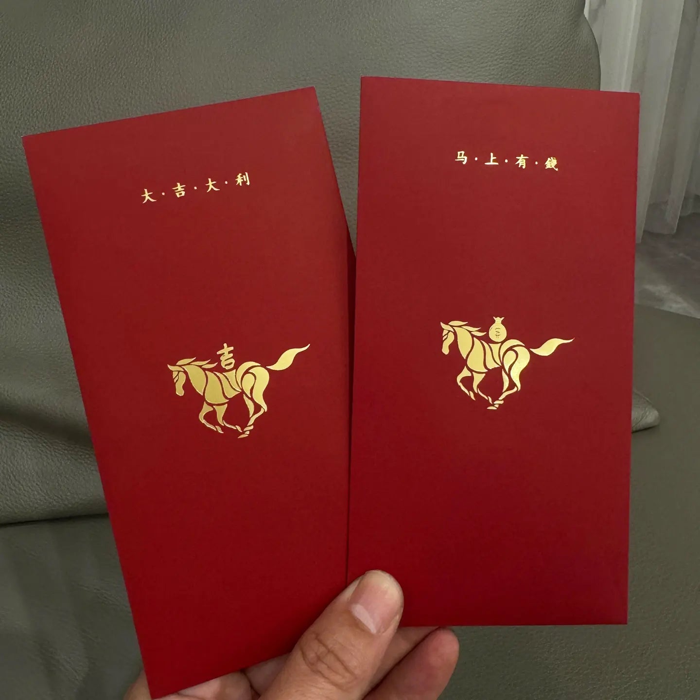 Two red envelopes with gold horse Minimalist 2026 Year of the Horse Red Envelopes - Lucky Money Packets held by a hand against a neutral background.
