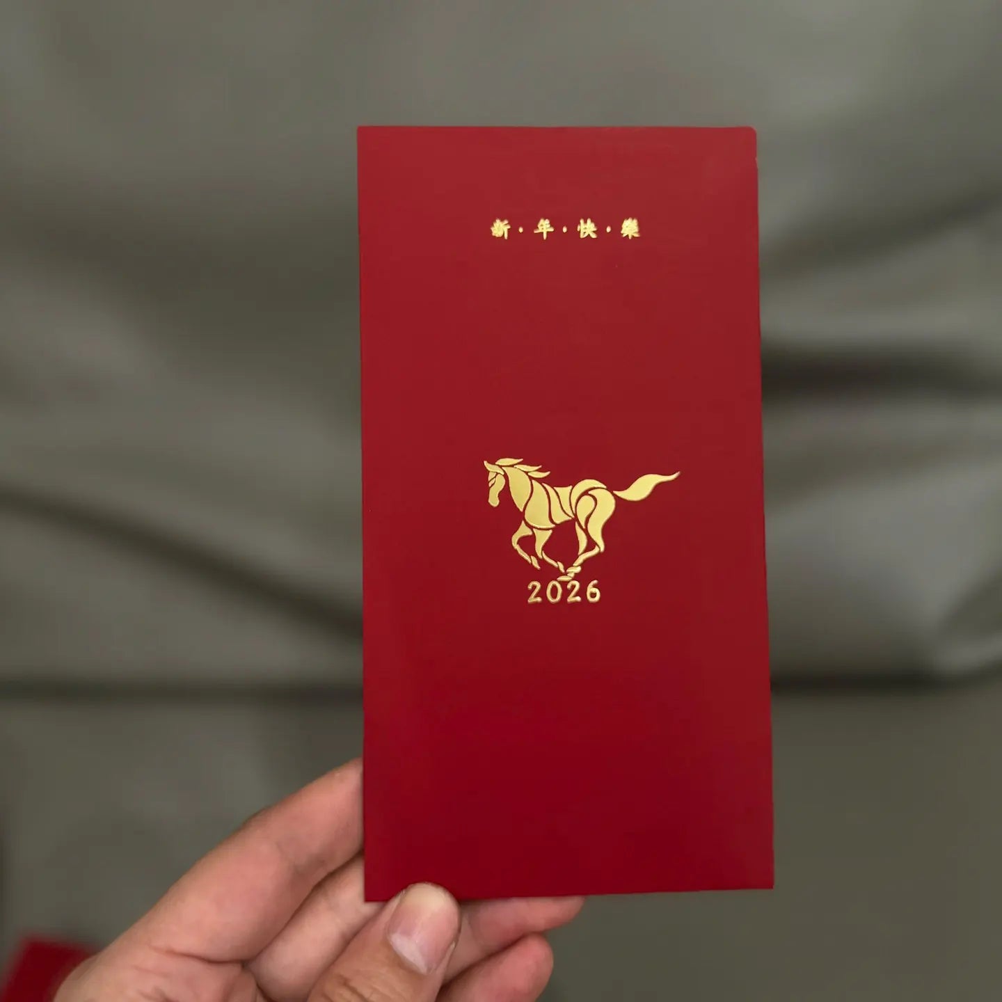 Minimalist 2026 Year of the Horse Red Envelopes - Lucky Money Packets  with gold horse design and '2026' text held by a hand against a gray background