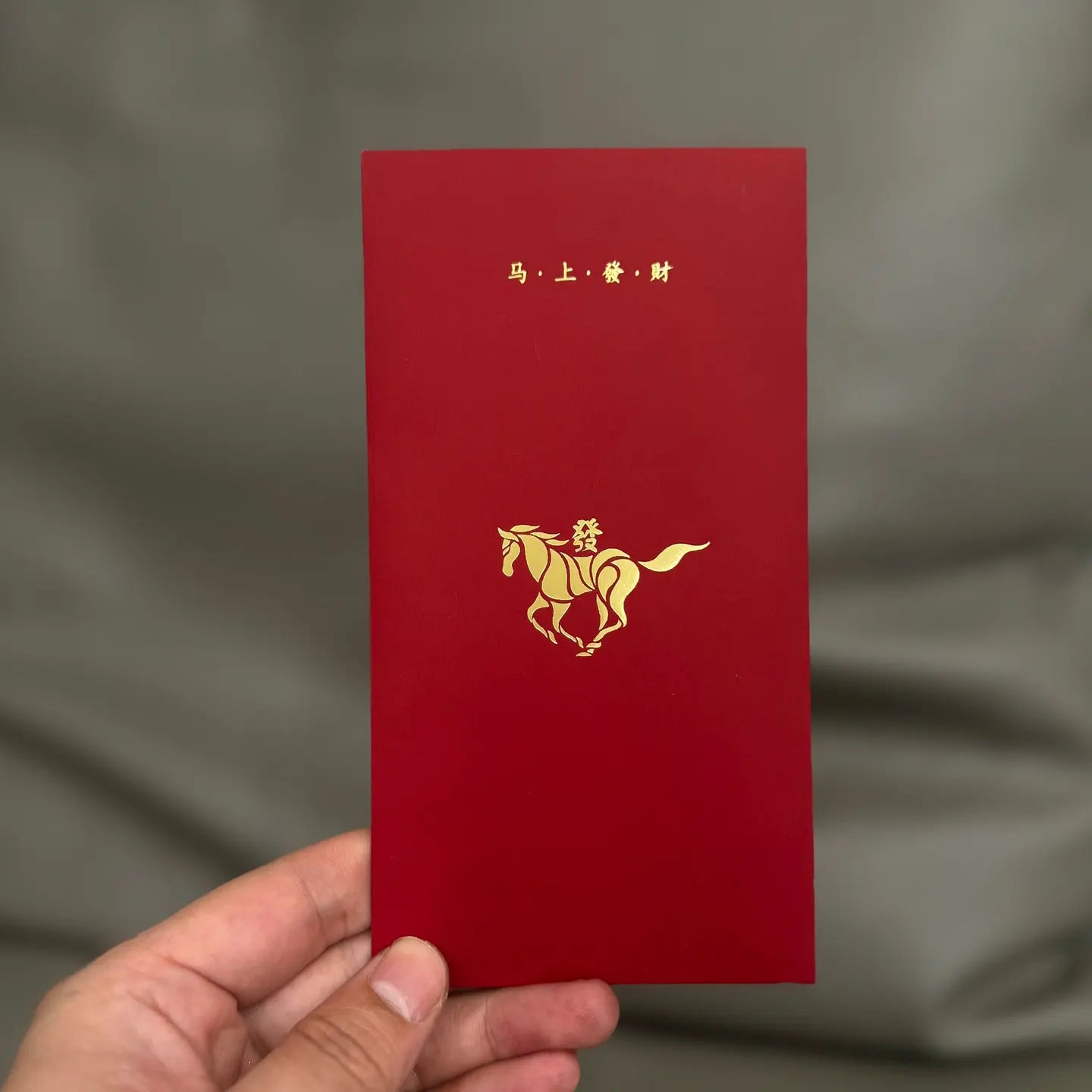 Minimalist 2026 Year of the Horse Red Envelopes - Lucky Money Packets  with gold horse design and Chinese text held by a hand against a gray background