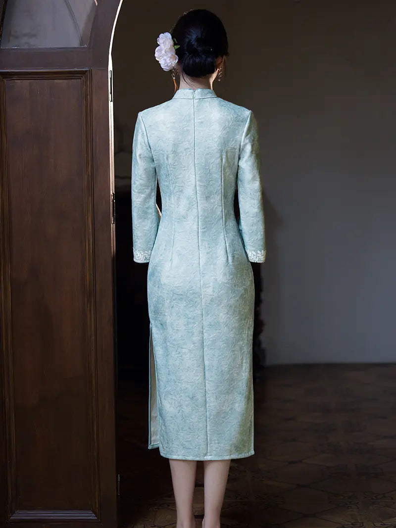 A woman viewed from behind wearing a light mint green textured cheongsam dress with long sleeves and a high collar, standing in a dimly lit interior next to a dark wooden door.