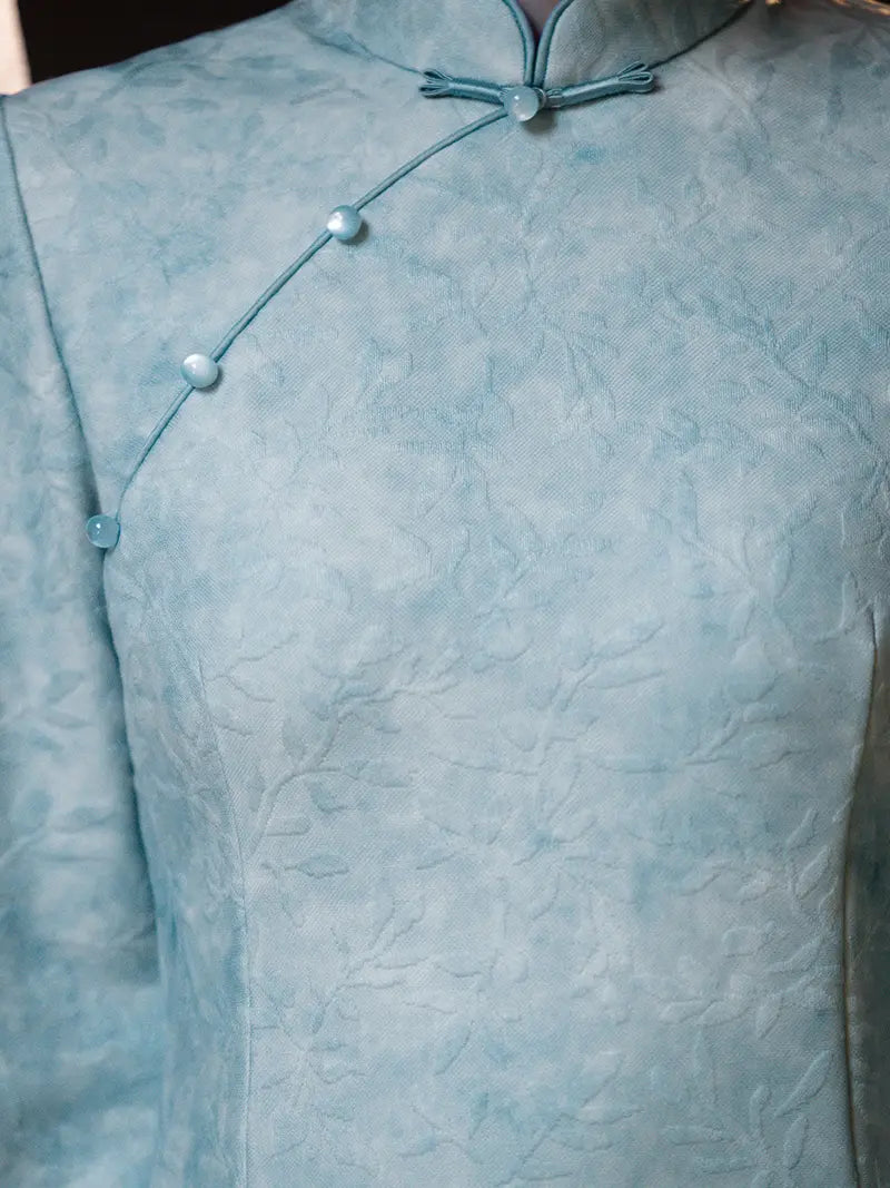 A close-up of a light blue textured fabric garment with a traditional collar and decorative front buttons.