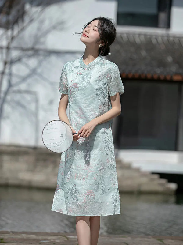 Woman in a light Mint Green Scenic Brocade Loose A Line Qipao Dress holding a round fan outdoors.