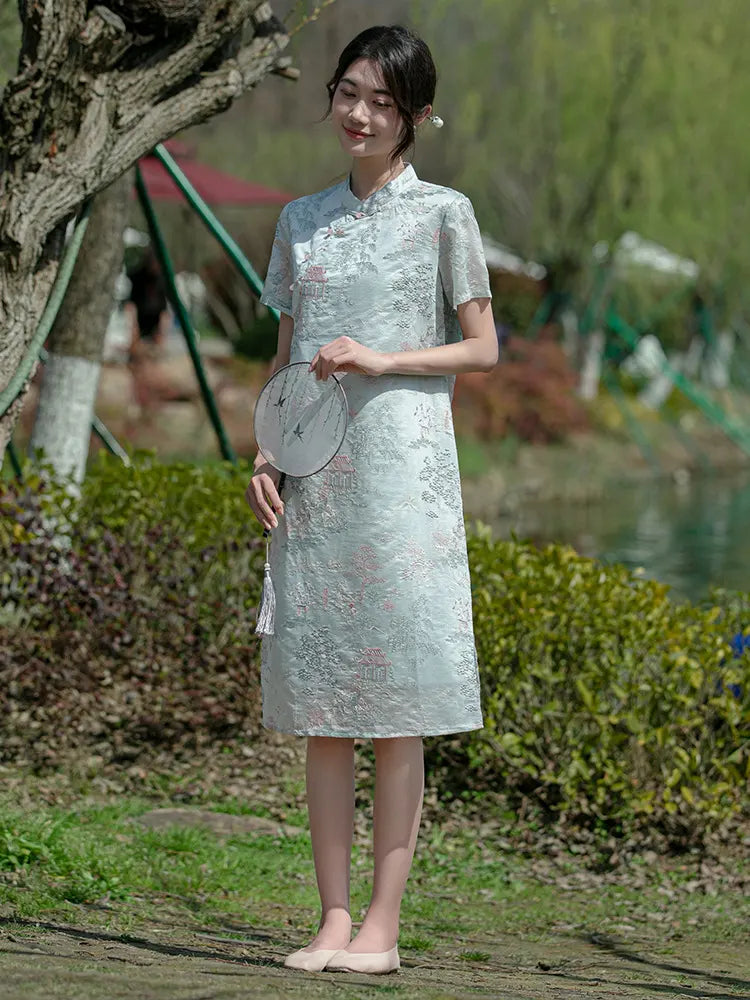 Woman in a light green traditional chinese a line qi pao cheongsam dress standing outdoors with trees and grass in the background 