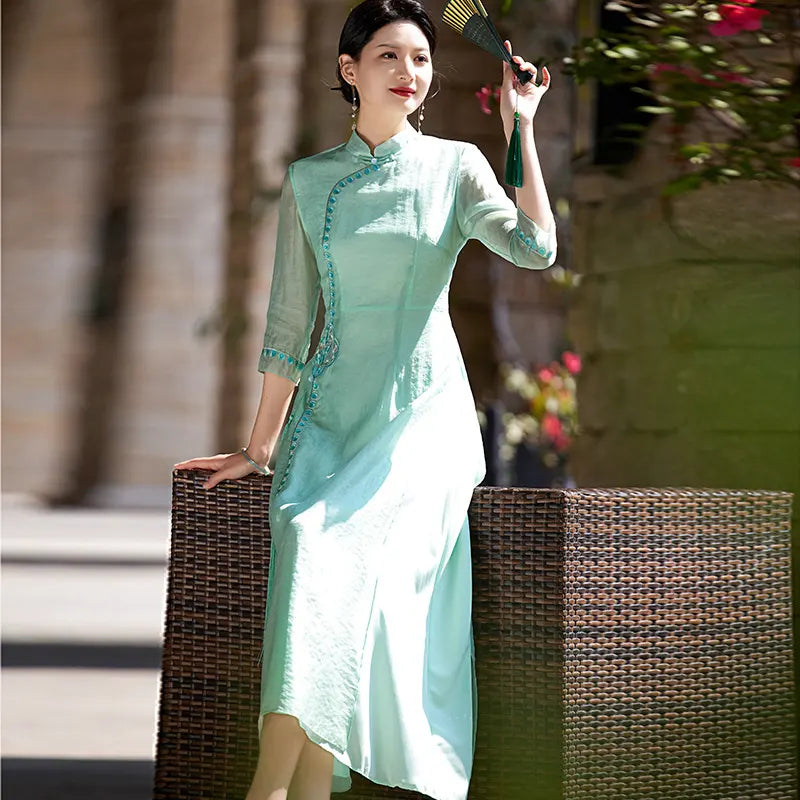 a chinese Woman in a green Modern A-Line Tencel Jacquard Loose Cheongsam Qipao Dress holding a fan, standing outdoors.