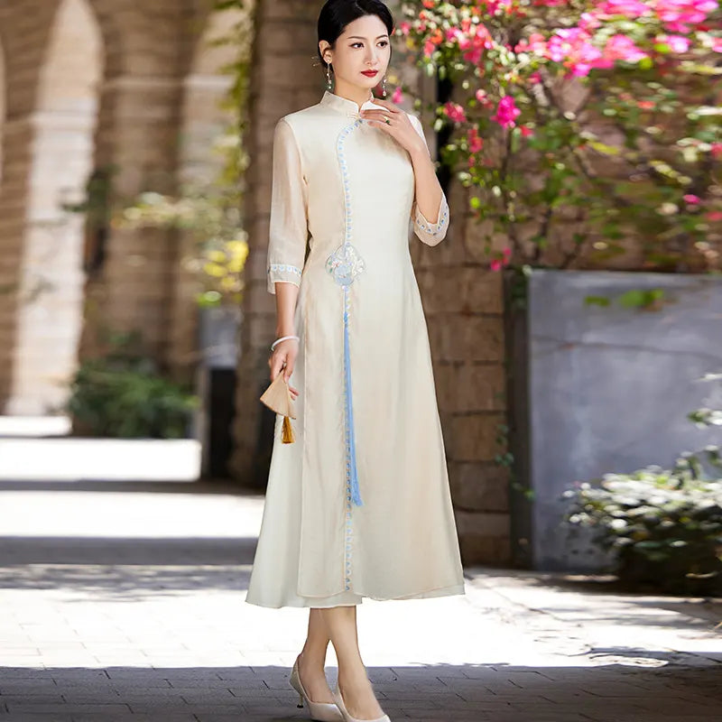 a chinese Woman in a long, beige Modern A-Line Tencel Jacquard Loose Cheongsam Qipao Dress standing outdoors with flowers in the background