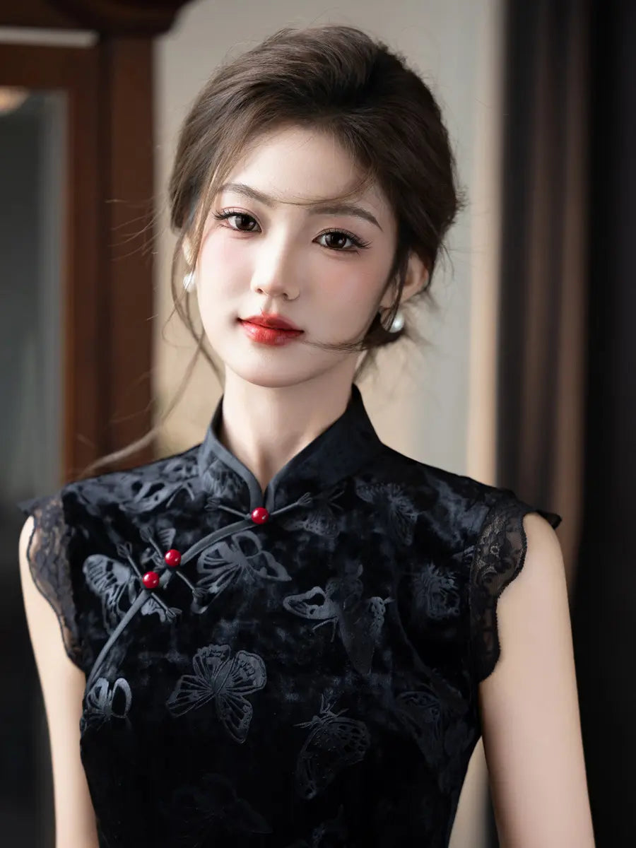 A woman wearing a black cheongsam with butterfly embroidery and red decorative accents, photographed indoors against a softly blurred background.