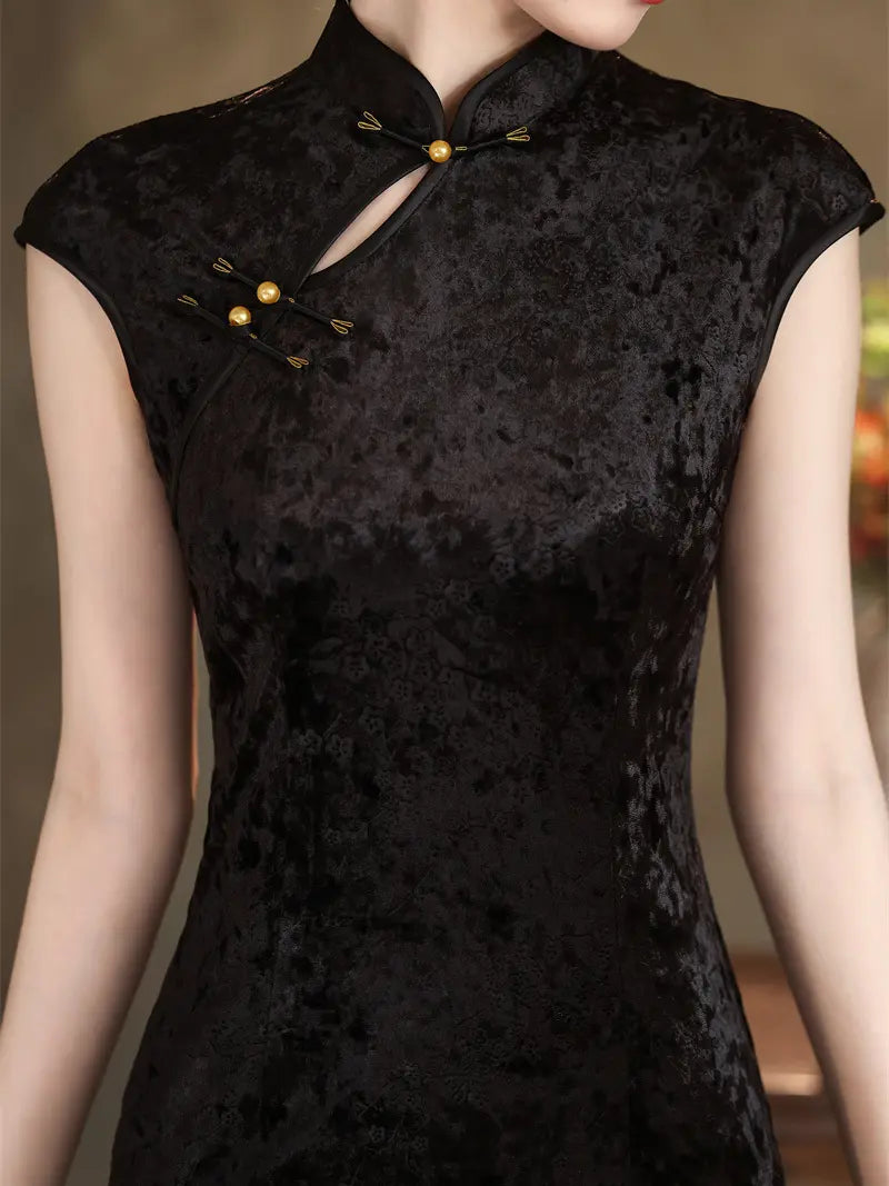 A close-up of a woman wearing a black textured cheongsam-style dress with gold-tone decorative buttons and a keyhole neckline.