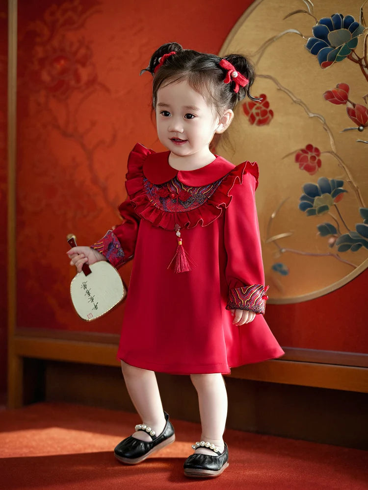 Young girl in a redModern Chinese Baby Qipao Cheongsam Dress with Tassel  standing in front of a decorative wall.