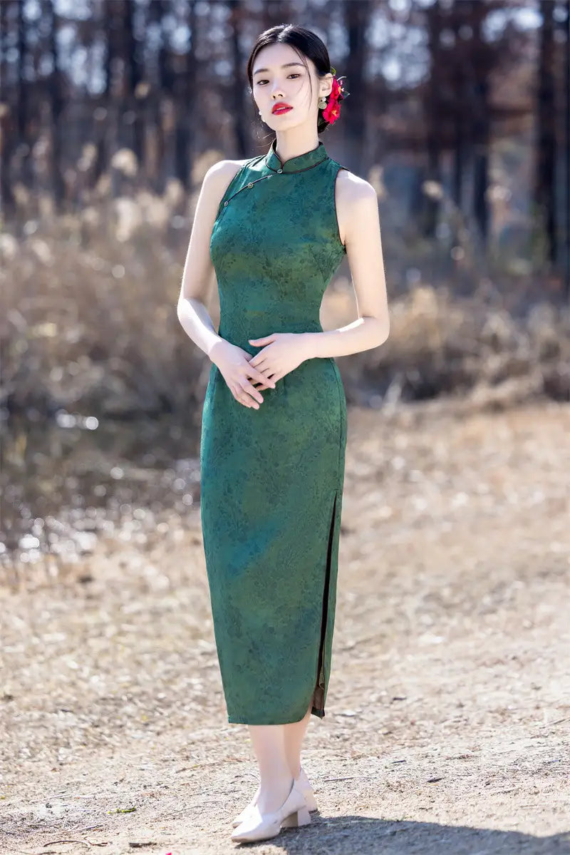 Woman in a green Modern Chinese Mandarin Dress Sleeveless Qipao  standing in a natural setting with trees and dry grass.