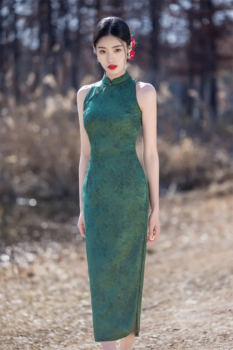 Woman in a green Modern Chinese Mandarin Dress Sleeveless Qipao  standing in a natural setting with trees and dry grass.