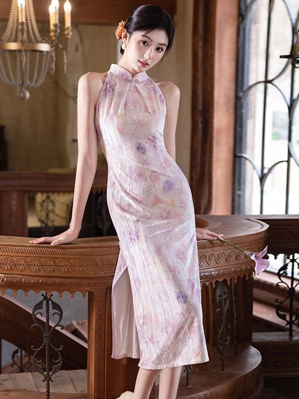 A woman wearing a sleeveless, high-neck, floor-length cheongsam dress with a light pink base and purple floral print, posing on a wooden staircase in a vintage-style interior.