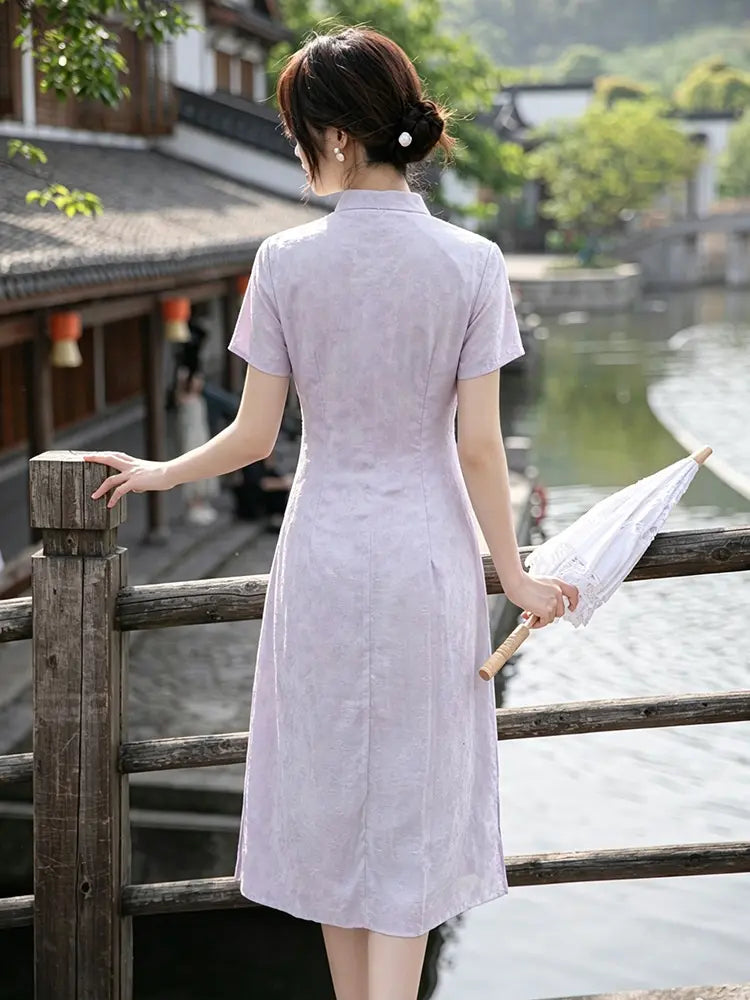 Woman in a light purple Modern Lavender A-line Short Sleeve Summer Qipao Dress  holding an umbrella, standing by a wooden railing with traditional architecture and a canal in the background.