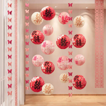 Red and pink hanging lanterns with Chinese characters double happiness and butterfly decorations displayed in a decorated indoor room.
