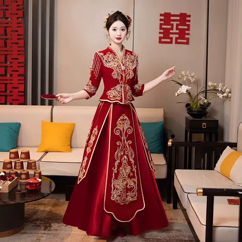 Woman in a red and gold Modern Red Qun Kwa / Xiuhe Chinese Wedding Gown  standing in a decorated room with floral decorations and a couch.